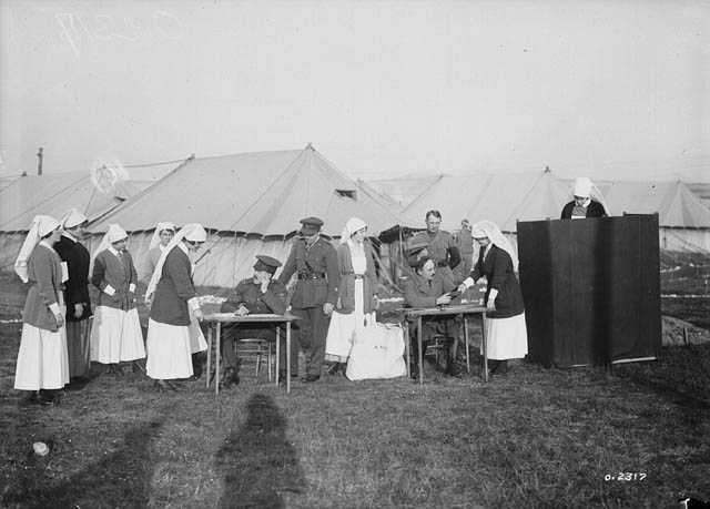 Black and white photograph. Nursing sisters in their uniforms line up at poll tables to vote near a tent.
